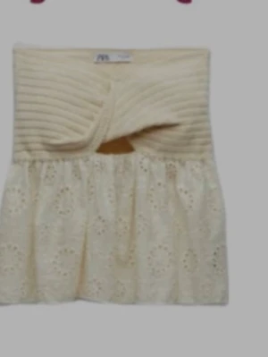 Krämvit bandeau topp med spetsdetaljer - Söt bandeau topp i krämvitt med ribbad överdel och twist framtill. Nedre delen har broderad spets med hålmönster som ger en romantisk vibe. Perfekt för varma dagar och att styla lager på lager.