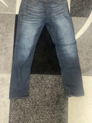 Jack & Jones Mörkblå raka jeans - Säljer ett par Jack & Jones jeans slim/ straight fit med snygga slitningar framtill. Jeansen har klassisk femficksdesign och kontrastsömmar baktill. Perfekta för en avslappnad och trendig look. Materialet är troligtvis bomullsdenim. Priset kan diskuteras.
