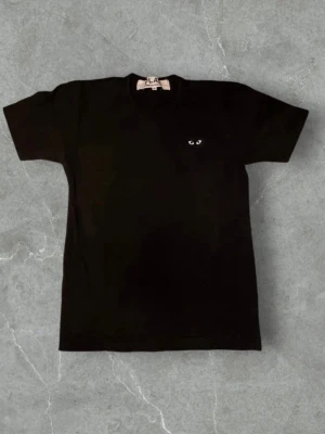 Svart t-shirt från Comme des Garçons Play L - Svart t-shirt från Comme des Garçons Play med det ikoniska hjärtat broderat på bröstet. Klassisk passform och rund halsringning. Perfekt plagg för en clean och stilren look. Storlek L men passar M. Passar dig runt 175-185 cm. Fint skick utan några defekter. Hör av er vid frågor och funderingar!