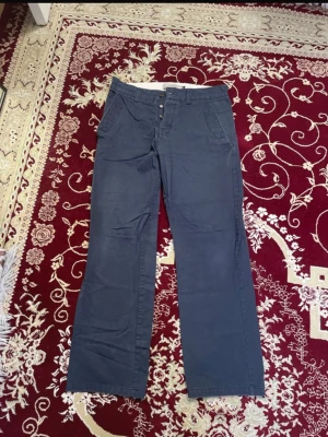 Marinblå Puma Chinos - Snygga marinblå chinos med raka ben och klassiska fickor fram från Puma. Byxorna har bälteshällor och stängs med knapp och dragkedja. 2 för 120 kr på alla herrbyxor. 