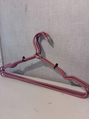5st rosa galgar - Säljer ett set med 5st rosa galgar med gummibeläggning för extra grepp. Galgarna har en modern design med mjuka former och svarta detaljer. Perfekta för att hänga kläder i garderoben.