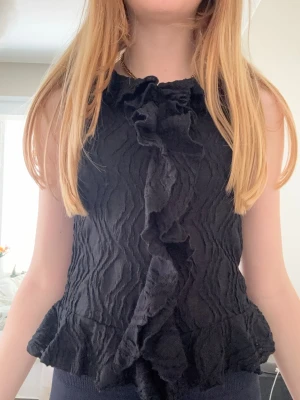 Svart volangblus med struktur - Säljer en svart ärmlös topp med volangdetaljer ifrån Gina Young. Passar bra till finare/fest tillfällen!🌻💕