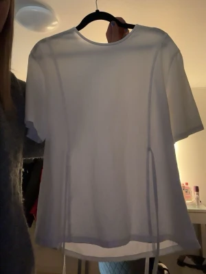 Vit t-shirt med snörning - Vit t-shirt i mjukt material med snörningsdetaljer på sidorna. Modellen har rund halsringning och korta ärmar. Passformen är normal och tyget ser ut att vara tunt och följsamt, perfekt för en clean och enkel look.