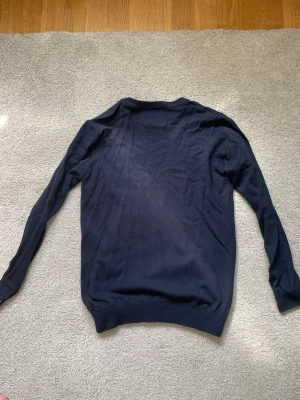 Mörkblå stickad tröja Jack & Jones - Mörkblå stickad tröja från Jack & Jones med rund halsringning och ribbade muddar vid ärmslut och nederkant. Tröjan har en enkel och stilren design, perfekt för lager på lager och funkar till det mesta. Materialet känns mjukt och lätt.