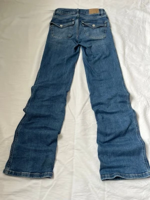 Low bootcut jeans från Lager 157 - Mörkblå bootcut jeans från Lager 156 med klassisk femficksdesign och snygga detaljer på bakfickorna. Jeansen har en lätt tvättad look och är tillverkade i mjuk denim med skön stretch. Perfekta för dig som gillar en avslappnad men trendig stil. Storlek XXS, Full längd. Diskuterar gärna pris! ✨
