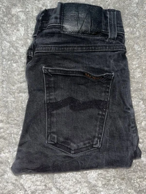 Nudie jeans  - Säljer ett par svarta skinny jeans från Nudie Jeans med klassisk femficksdesign och råa, avklippta benslut. Jeansen har en diskret logga på bakfickan och är tillverkade i stretchigt denimtyg för en bekväm passform. OBS uppklippta så är ej L32 utan mer som L28 men utgå från måtten. JAG KAN EJ HA JEANSEN SÅ KAN EJ SKICKA BILD NÄR JAG BÄR DOM så googla på modellnamnet för att se passform. S6