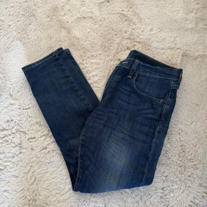 Mörkblå Levi's jeans straight fit - Klassiska mörkblå jeans från Levi's med straight fit och fem fickor. Jeansen har en diskret tvättad look och läderpatch bak i midjan. Perfekta för en avslappnad och stilren outfit.