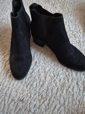 Svarta Chelsea boots i mocka - Snygga svarta Chelsea boots i mocka med klassisk resår på sidorna och låg klack. Bootsens stilrena design gör dem perfekta till många olika outfits. De har rundad tå och diskret sula. Märke syns ej tydligt på bilden.