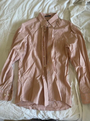 Rutig skjorta från Gant i orange och vit storlek L - Säljer en snygg rutig skjorta från Gant i orange och vitt. Skjortan har klassisk krage, långa ärmar och knappar framtill. Regular fit-modell i mjuk bomull som passar perfekt till jeans eller chinos.