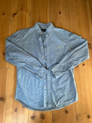 Blå skjorta från Polo Ralph Lauren - Klassisk ljusblå skjorta från Polo Ralph Lauren i slim fit-modell. Skjortan blir perfekt nu till sommarn när de blir så varmt ☀️den har en defekt i vänstra armhålan men går säkert att tvätta bort annars är den stilren. Tveka inte om att höra av er!🌟