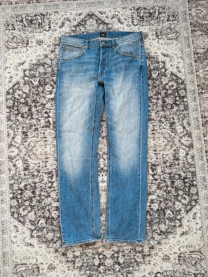 Blå jeans Lee - Snygga blå jeans från Lee med raka ben och klassisk femficksdesign. Jeansen har slitningar och ljusare partier framtill samt Lee-lapp bak i midjan. Perfekta för en avslappnad och trendig look. För mer info skriv gärna 🙌