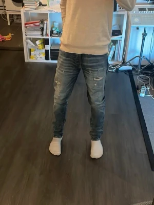 Jack and Jones jeans - Säljer ett par blå jeans med slitningar och lätt tvättad look. Jeansen har normal midja och smal passform, perfekta för en avslappnad stil. Klassisk femficksmodell och dragkedja i gylfen. Passar dig som gillar en trendig och casual vibe.