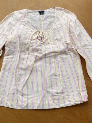 Randig blus med trekvartslånga ärmar från Gant i nyskick. Storlek 36.  - Söt blus från Gant med pastellfärgade ränder i rosa, lila och vitt som jag fått i present men aldrig använt. Storlek 36. Blusen har rund halsringning med liten rosett och trekvartsärm. Tillverkad i ett lätt och luftigt bomullstyg, perfekt för vår och sommar.