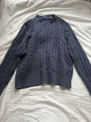 Mörkblå  tröja Ralph Lauren - Kabelstickad mörkblå tröja från  Ralph Lauren med rund halsringning och ribbade muddar. Vid funderingar är det bara att höra av sig :)