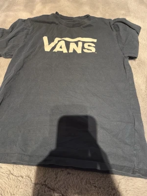 Blå  VANS t-shirt med logga - Blå  t-shirt från VANS med stor vit logga på bröstet. Klassisk passform och rund halsringning, perfekt för en avslappnad streetstyle-look.