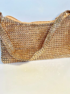 Partyväska med strass stenar  - Väska med mjuk passform dragkedja och kortare band. Strass stenar i färgen champagne . En perfekt Partyväska 