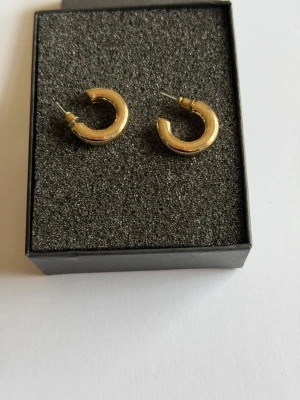 Guldiga chunky hoops örhängen - Snygga guldiga hoops örhängen i chunky design. De är runda och har en blank, polerad yta som ger ett stilrent intryck. Perfekta för dig som gillar minimalistiska men ändå statement smycken. Materialet ser ut att vara metall med guldfinish.