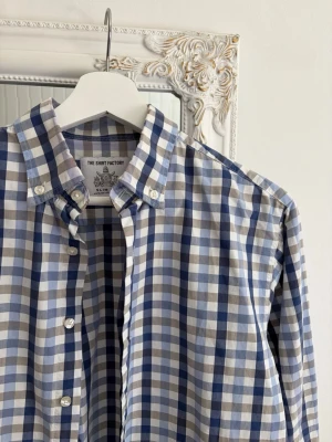 Rutig skjorta från the Shirt Factory - Säljer en riktigt schysst rutig skjorta från the Shirt Factory. Storlek 39 och passar mig som vanligtvis kör medium i kläder. Skjortan är i riktigt fint skick förutom i kragen där det finns lite tecken på användning (se bilden).