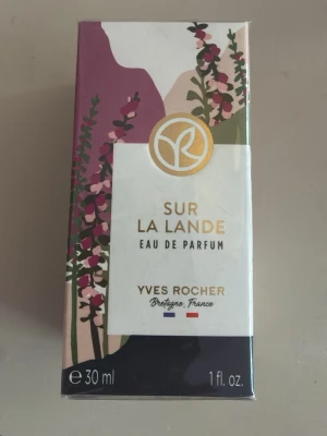 Yves Rocher Sur La Lande Parfym 30ml - Sur La Lande Eau de Parfum från Yves Rocher, 30 ml. Parfymen har en blommig, orientalisk och mineralisk doft med inslag av vilda blommor och havsalger. Förpackningen är dekorerad med blommönster i lila, grönt och vitt samt gulddetaljer.