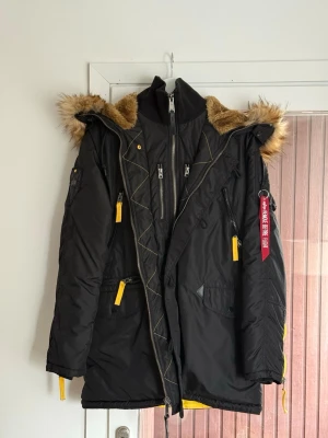Alpha Industries parkas  - Säljer min killes jacka från Alpha Industries. Den är i jättefint skick, enda defekten är att en knapp vid luvan har lossnat (se bild) men går nog att fixa till/sy fast! 