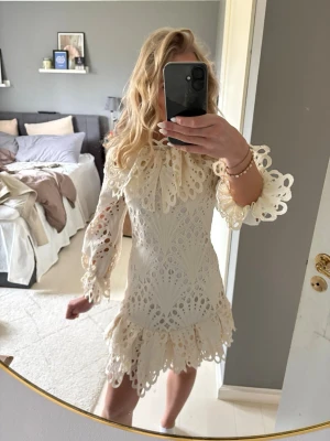 Vit spetsklänning med volang - Superfin vit kortklänning med spetsdetaljer och volang vid ärmslut och nederkant. Klänningen har långärmade ärmar med vackra broderade mönster