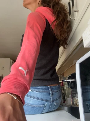 Svart och rosa tröja från Puma - Säljer en snygg hoodie från Puma med svart kropp och rosa ärmar och huva. Tryck på bröstet med texten 'Authentic Sporting Goods' och Puma-logga. Mjuk bomullsblandning, känguruficka framtill och ribbade muddar. Passar Xs!! Perfekt för en sportig och avslappnad men också vintage stil.