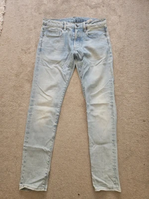 Ljusblå slim fit jeans - Snygga ljusblå slim fit jeans med klassisk femficksdesign och diskreta slitningar på benen. Jeansen har en läderpatch bak i midjan och raka ben. Perfekta för en avslappnad och trendig look.