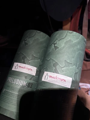 Mackmyra Preludium 03 whiskyförpackning - Två gröna cylinderformade förpackningar från Mackmyra för Preludium 03 Svensk Single Malt Whisky. Förpackningarna har ett mönster i olika gröna nyanser och tydlig etikett med logga och text. Perfekt för whiskyentusiasten eller samlaren.