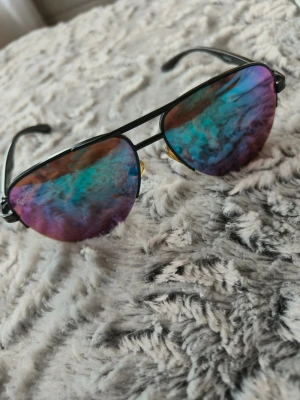 Ray-Ban aviator solglasögon färgade glas - Säljer ett par klassiska Ray-Ban aviator solglasögon med spegelglas i blå, lila och gröna toner. Bågarna är svarta. Perfekt accessoar för dig som vill sticka ut med färgstarka glas och tidlös design.har använda lite inga fel som ny