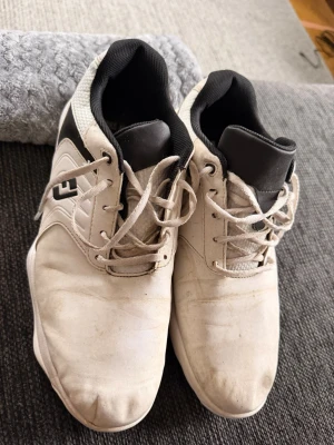 Vita golfsneakers från FootJoy - Säljer ett par vita sneakers från FootJoy med svart detalj och logga på sidan. Skorna har snörning, svart vadderad plös och krage samt ovandel i syntetmaterial och mesh. Snygg sportig look som funkar till många stilar.