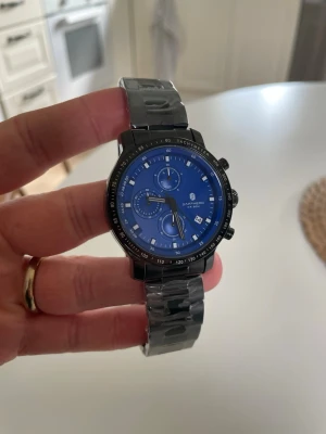 Klocka, helt ny!  - Stilren klocka från Sapphero med blå urtavla och svart stål. Klockan har kronograffunktion, datumvisning och tydliga markeringar runt urtavlan. Klockan är helt ny och har fortfarande plasten kvar. 