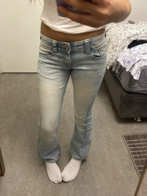 Ljusblå bootcut jeans med slitningar - Säljer ett par ljusblå bootcut jeans med snygga slitningar och klassiska femficksdetaljer. Jeansen har en låg midja och är tillverkade i denim med stretch för skön passform. Perfekt för dig som gillar en avslappnad och trendig look.
