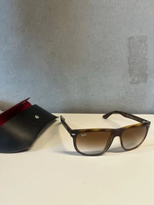 Bruna Ray-Ban solglasögon - Bruna solglasögon från Ray-Ban med klassisk fyrkantig form och tonade glas. Bågarna är i plast och har Ray-Ban-loggan på sidan. Kommer med svart fodral med röd insida.