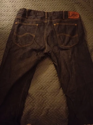 Mörkblå jeans från Lee - Säljer ett par klassiska mörkblå jeans från Lee med raka ben och snygga kontrastsömmar. Jeansen har två bakfickor med Lee-logga på läderpatch och två framfickor. Materialet är slitstark denim i bomull.