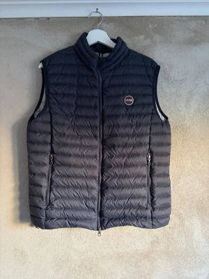 Svart dunväst från Colmar - Snygg svart dunväst från Colmar med quiltad design och hög krage. Västen har två dragkedjeförsedda fickor framtill och en diskret logotyp på bröstet. Perfekt för lager-på-lager och håller dig varm utan att bli klumpig.