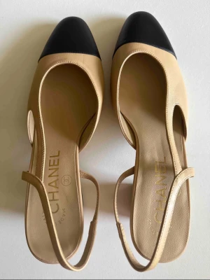 cc slingbacks  - Stilrena klackskor i beige läder med svart tå och öppen häl. Skorna har en låg klack med diskret logga och smal rem runt hälen. Klassisk tvåfärgad design som ger en tidlös look. Klack 6.5cm