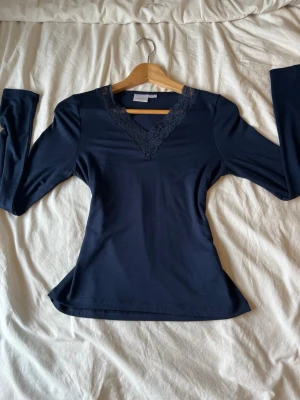 Mörkblå långärmad topp med spets - Mörkblå långärmad topp från Gina Tricot med v-ringning och dekorativ spets runt halsen. Toppens material känns mjukt och stretchigt, perfekt för en stilren look. Passformen är normal och toppen har en feminin touch tack vare spetsdetaljerna. Den är i storlek 158-164 (ca XS) och ALDRIG ANVÄND!!