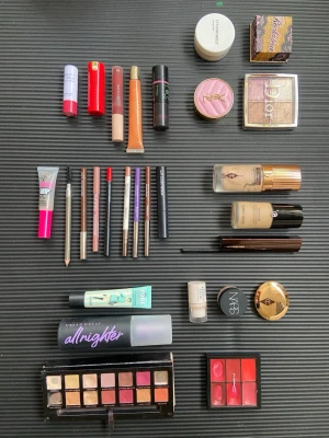Makeupkit med basprodukter och paletter - Stort makeupkit med flera basprodukter som foundation, concealer, puder, highlighter, bronzer och setting spray från märken som Charlotte Tilbury, Urban Decay, Benefit, NARS och Dior. Innehåller även ögonskuggspalett, läpprodukter och pennor i olika färger och former.