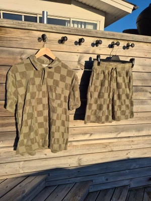 Grön-rutig t-shirt med tillhörande shorts - Säljer en grön t-shirt med rutigt mönster och krage samt matchande shorts. Båda i ett frottéliknande material. Använda vid ett fåtal tillfällen.