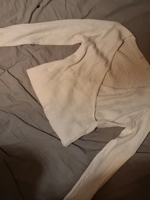 Vit ribbad omlottkofta - Säljer en vit ribbad omlottkofta med långa ärmar. Koftan har en croppad passform och är tillverkad i ett mjukt, stretchigt material. Perfekt att styla över ett linne eller topp för en trendig look.