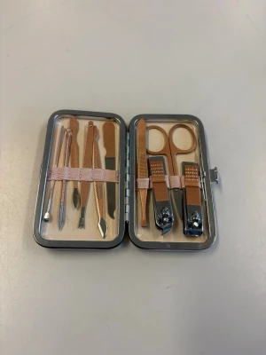 Manikyrset i roséguld med fodral - Ett komplett manikyrset i roséguld med flera verktyg för nagelvård, inklusive nagelsax, nagelklippare, fil, nagelbandsskärare och pincett. Verktygen är tillverkade i metall och kommer i ett smidigt fodral med rosa band för enkel förvaring.