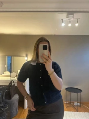 Mörkblå kortärmad kofta med pärlknappar - Säljer en mörkblå, kortärmad kofta med pärlknappar framtill. Koftan är stickad i ett fluffigt material och har en rund halsringning. Ny med prislapp. Storlek M men passar även mindre. Nypris 399kr