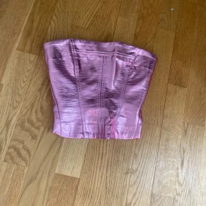 Rosa fest korsettopp från Bershka - Säljer en glansig rosa metallic korsettopp från Bershka. Toppen har dragkedja bak och markerade sömmar för en snygg passform. Storlek xs. Använd en gång🩷