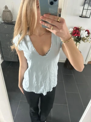 Ljusblå v-ringad topp från Zara - Säljer en ljusblå topp från Zara med v-ringning och korta ärmar. Toppen är i mjuk bomull och har en avslappnad passform som är perfekt till jeans eller kjol. Enkel och stilren design som passar till många olika looks. OBS! Tröjan är i avklippt modell i v-ringning, ärmar och nertill