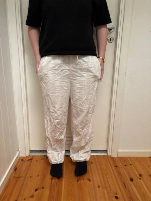 Vita linnebyxor med resårmidja - Säljer ett par vita linnebyxor med avslappnad passform och resår i midjan. Byxorna har raka ben och sidofickor, perfekta för en chill och luftig stil. Materialet är 100% linne vilket gör dem svala och sköna. jag har använt dem som pyjamas byxor