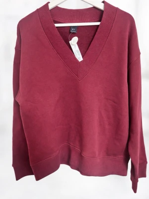 Vinröd V-ringad sweatshirt Lindex - Vinröd sweatshirt från Lindex med djup V-ringning och breda muddar vid ärmslut och nederkant. Tillverkad i mjuk bomullsblandning och har en avslappnad passform. Perfekt för en chill och stilren look.