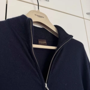 Rose & Born - 5 500kr Rose & Born kofta i 100 % kashmir – mörkblå Elegant kofta i finstickad kashmir från exklusiva Rose & Born. Klassisk passform med hel dragkedja och ribbade muddar. En tidlös garderobsklassiker som kombinerar lyx och stil.