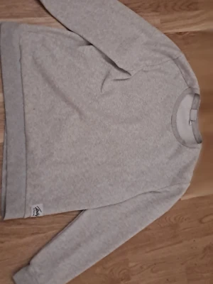 Ljusgrå sweatshirt från Franklin - En stilren ljusgrå sweatshirt från Franklin med rund halsringning och långa ärmar. Tröjan har en liten diskret logga nere vid fållen och är gjord i mjukt bomullsmaterial. Perfekt för en avslappnad look och enkel att matcha med jeans eller joggers.