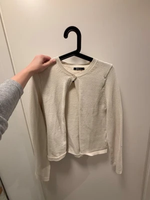 Krämvit kofta från Gina Tricot - Stilren krämvit kofta från Gina Tricot med rund halsringning och lång ärm. 