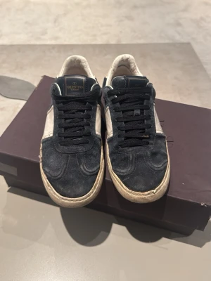 Svarta sneakers från Valentino - Snygga svarta sneakers från Valentino med vita detaljer och svart mocka. Klassisk låg modell med svart snörning och vit sula. Märkeslogga på plösen och stilren design som passar till det mesta.